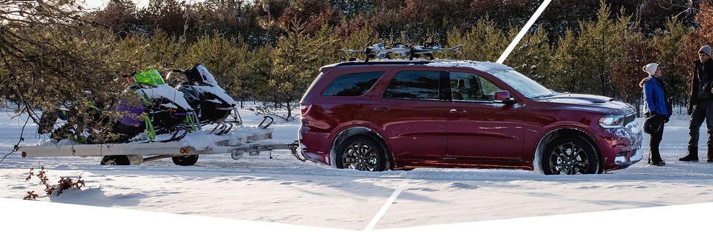 The 2021 Dodge Durango R/T parked on a snowy trail with an attached trailer with two snowmobiles on it.