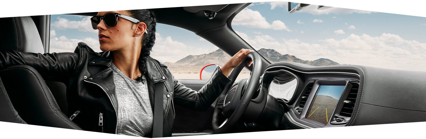 A driver in a 2020 Dodge Challenger looking behind the vehicle as the rear camera image is displayed on the touchscreen.