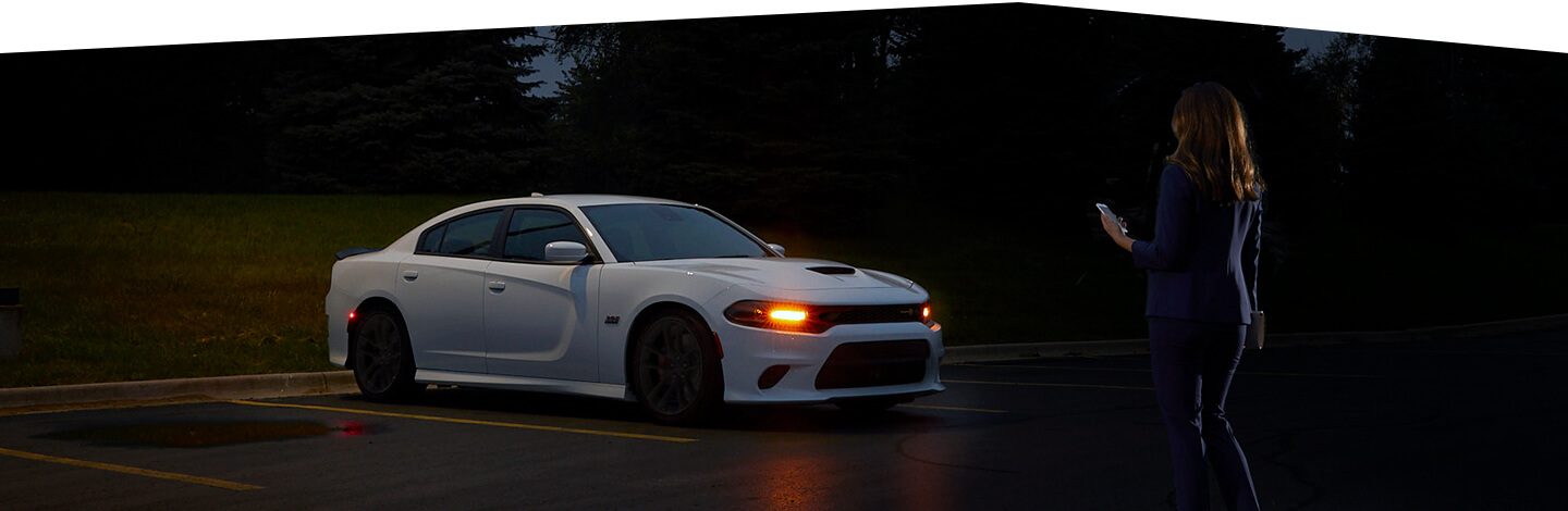 A woman approaching a 2020 Dodge Charger at night with its headlamps illuminated.